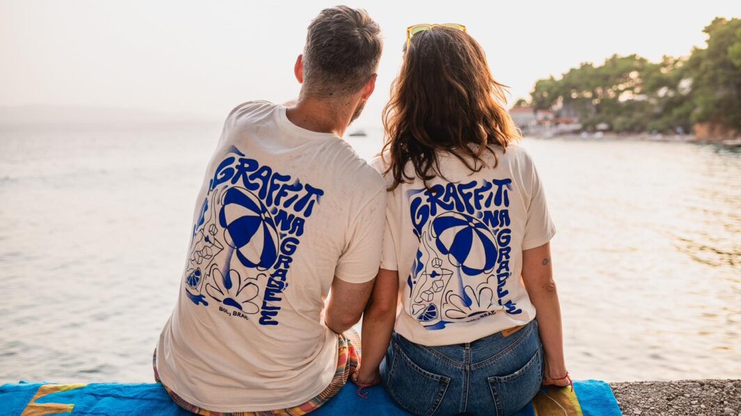 Boy and girl sitting on the coast, dressed in Graffiti na Gradele merchandise